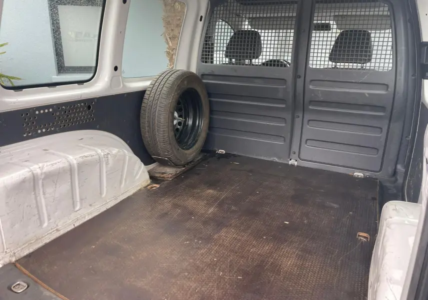 Vue intérieure arrière du Volkswagen Caddy blanc Candy 2014, montrant l'espace de chargement avec roue de secours fixée à gauche.