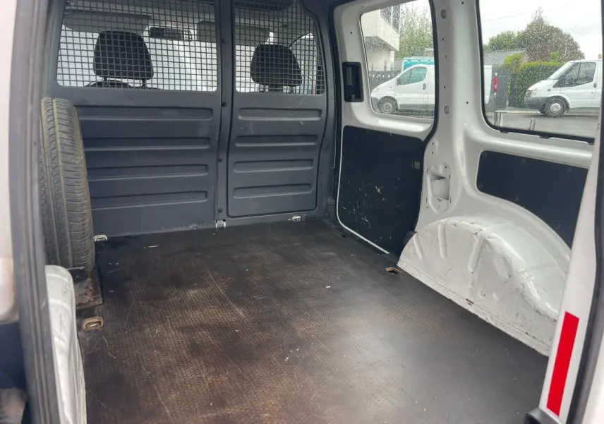 Vue intérieure arrière du Volkswagen Caddy blanc Candy montrant l'espace de chargement avec roue de secours fixée à gauche.