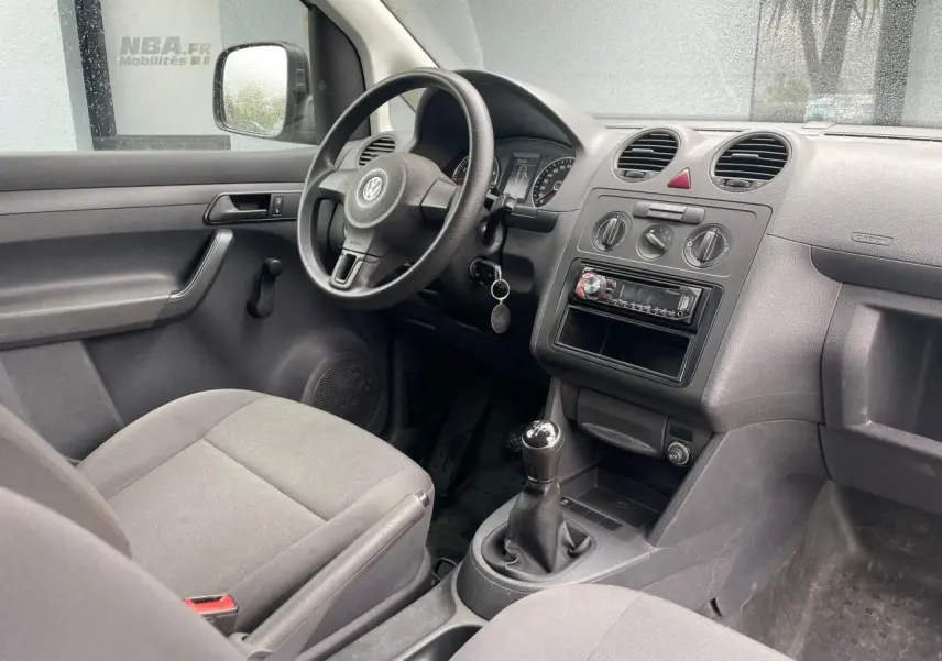 Intérieur du Volkswagen Caddy 2014 vu côté conducteur, tableau de bord gris avec boîte manuelle et volant noir.