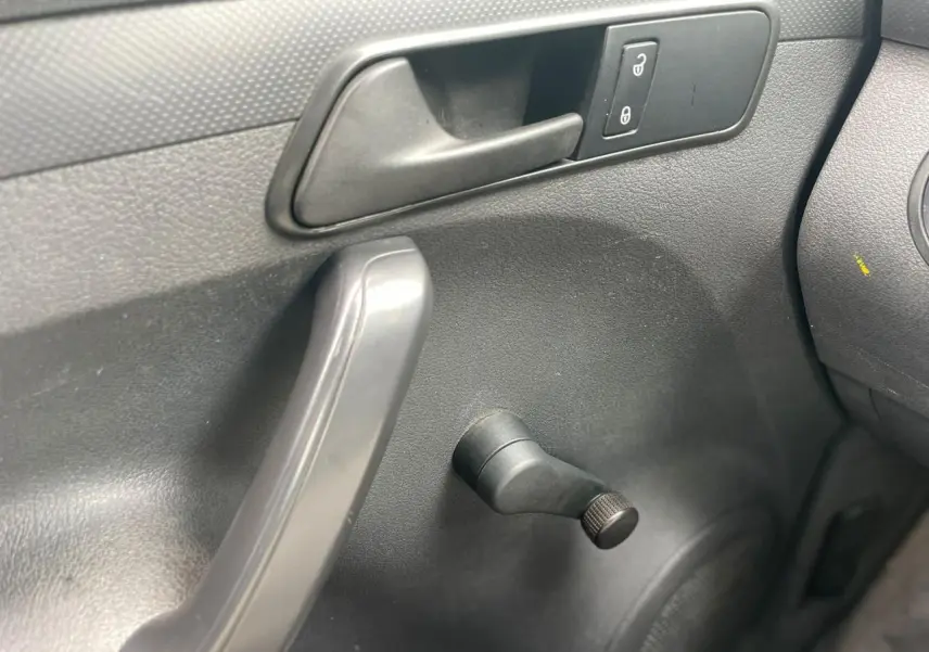 Détail de la manivelle de lève-vitre côté conducteur du Volkswagen Caddy blanc Candy 2014, intérieur noir.