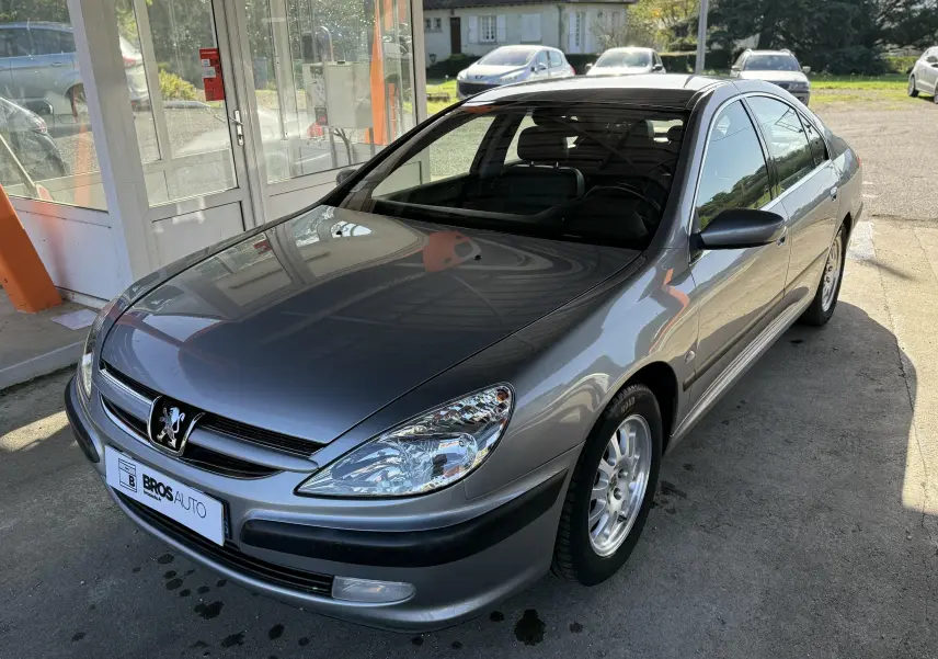 Peugeot 607 gris vue 3/4 avant droit, avec calandre noire et jantes alliage argentées.