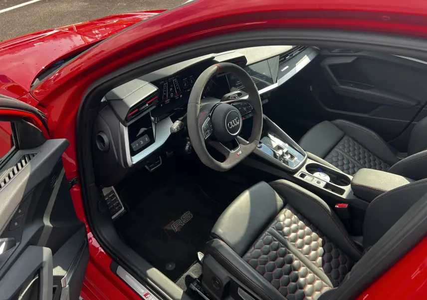 Vue intérieure côté conducteur de l'Audi RS3 Sportback rouge 2022, sièges cuir noir à surpiqûres rouges et volant sport.