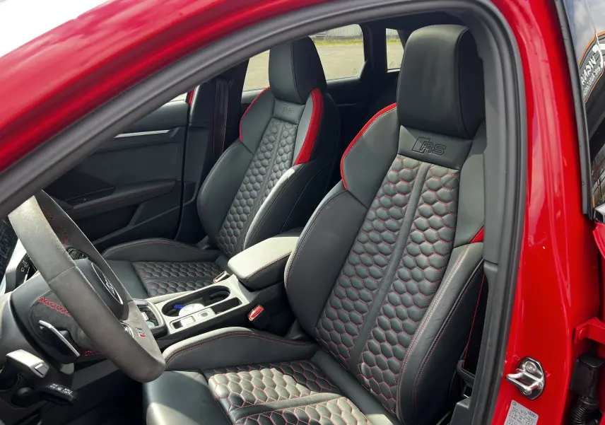 Vue intérieure côté conducteur de l'Audi RS3 Sportback rouge, sièges en cuir noir avec surpiqûres rouges et logo RS brodé.