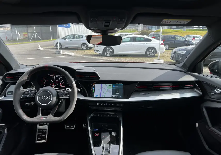 Vue intérieure de l'Audi RS3 Sportback 2022 avec tableau de bord noir, volant sport et écran tactile central affichant la navigation.