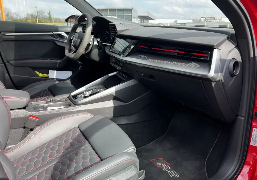 Intérieur côté passager de l'Audi RS3 Sportback rouge 2022 avec sièges cuir noir à surpiqûres rouges et tapis RS.
