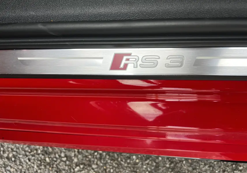 Gros plan sur la plaque de seuil de porte rouge d'une Audi RS3 Sportback avec logo RS3 en métal brossé.