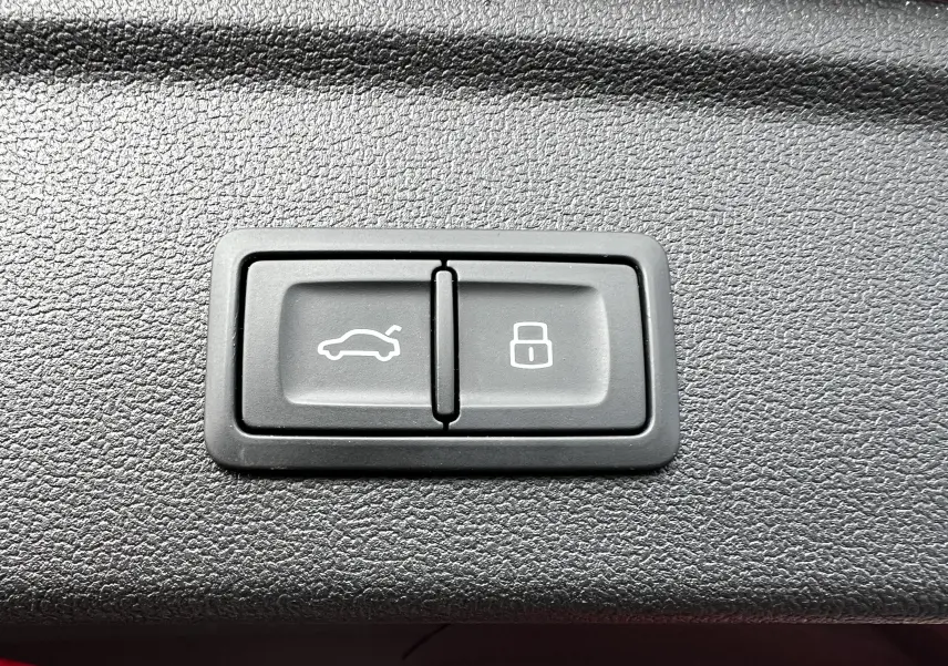 Boutons de commande pour ouverture du coffre et verrouillage, situés sur la garniture intérieure d'une Audi RS3 Sportback rouge 2022.