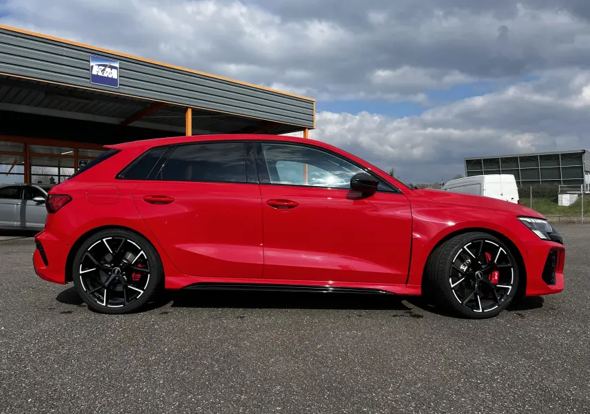 Audi RS3 Sportback rouge vue de profil côté gauche, avec jantes noires et étriers de frein rouges visibles.