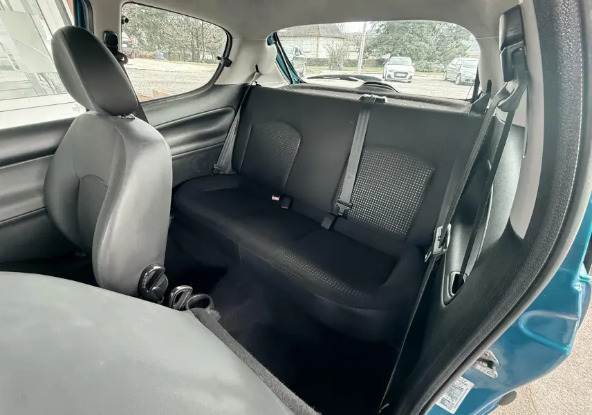 Vue intérieure arrière droite de la Peugeot 206+ bleue, montrant la banquette arrière en tissu noir et la portière ouverte.