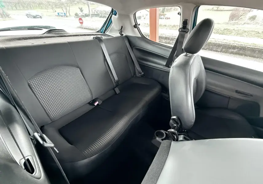 Vue intérieure arrière côté droit de la Peugeot 206+ 1.1 i 60 avec sièges tissu noir et ceintures de sécurité visibles.