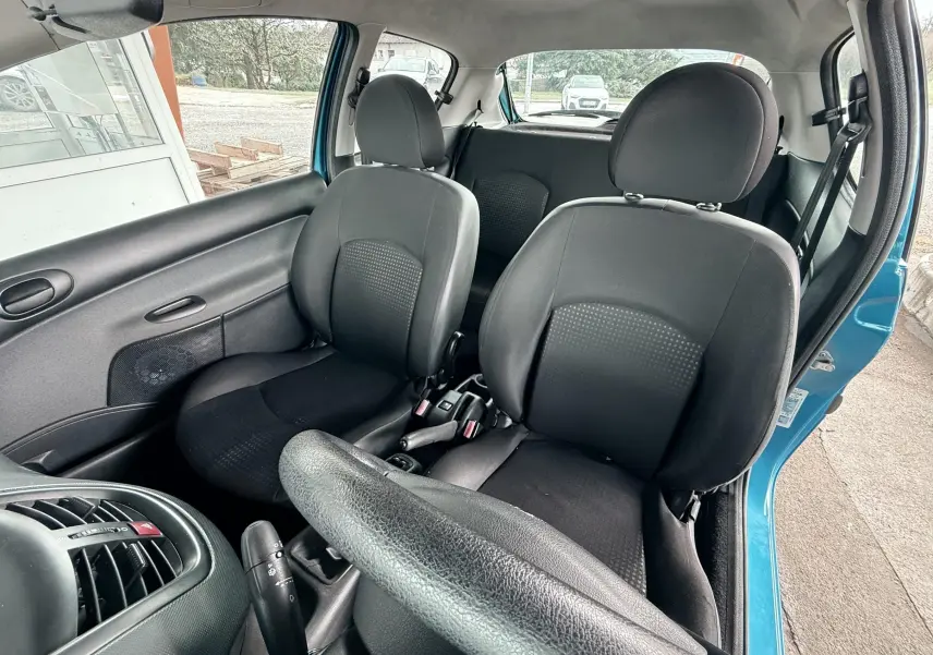Vue intérieure avant droite de la Peugeot 206+ bleue de 2011, montrant les sièges noirs en tissu et cuir et le volant.