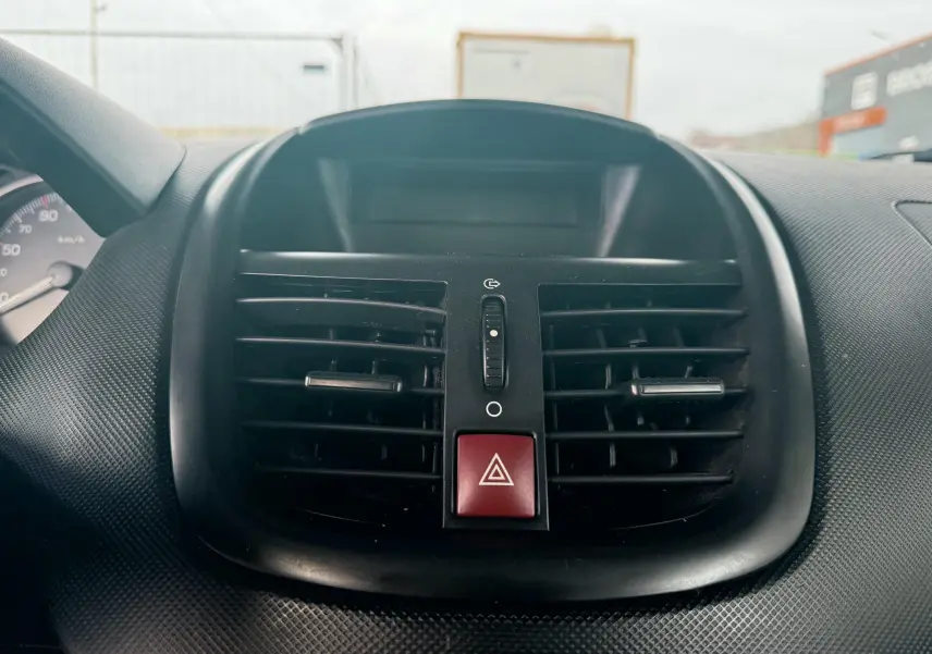 Vue rapprochée du tableau de bord de la Peugeot 206+ 2011, mettant en valeur les aérateurs centraux et le bouton de warning rouge.