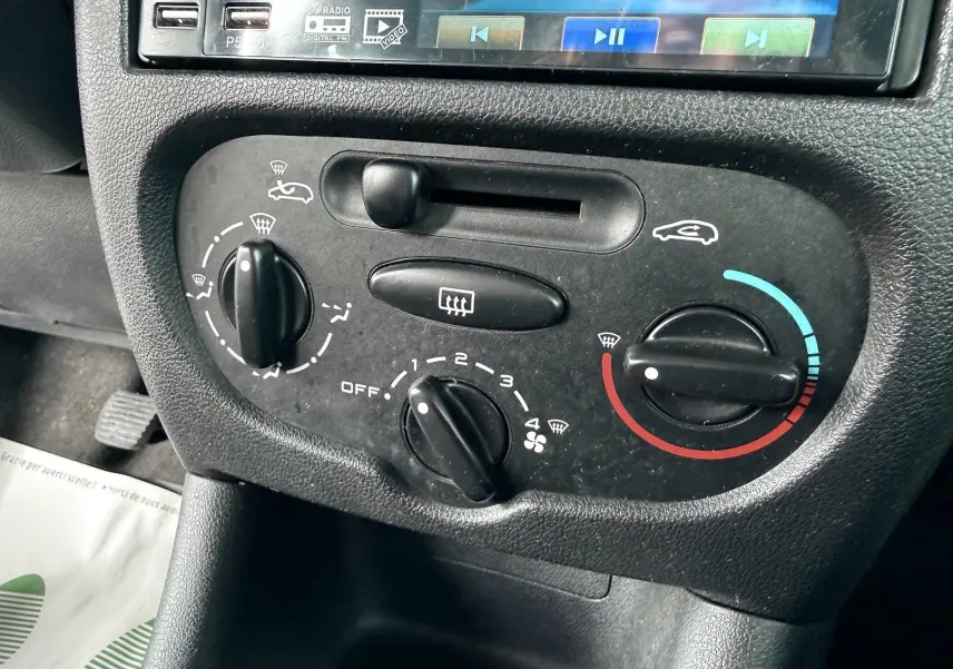 Détail de la console de climatisation noire de la Peugeot 206+ 1.1 essence, avec commandes rotatives et écran multimédia partiel.