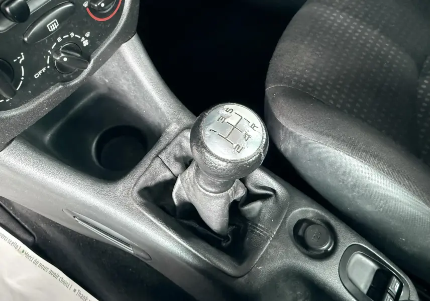 Gros plan sur le levier de vitesses manuel et la console centrale noire du Peugeot 206+ bleu, siège tissu visible à droite.
