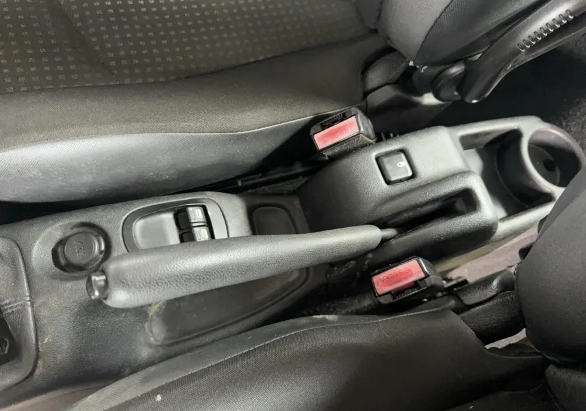 Vue rapprochée de la console centrale noire avec frein à main, boutons de lève-vitres et ceintures de sécurité rouges.