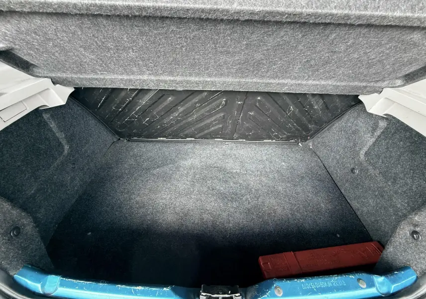 Coffre ouvert vu de face d’une Peugeot 206+ bleu, montrant un espace vide avec un triangle de signalisation rouge.