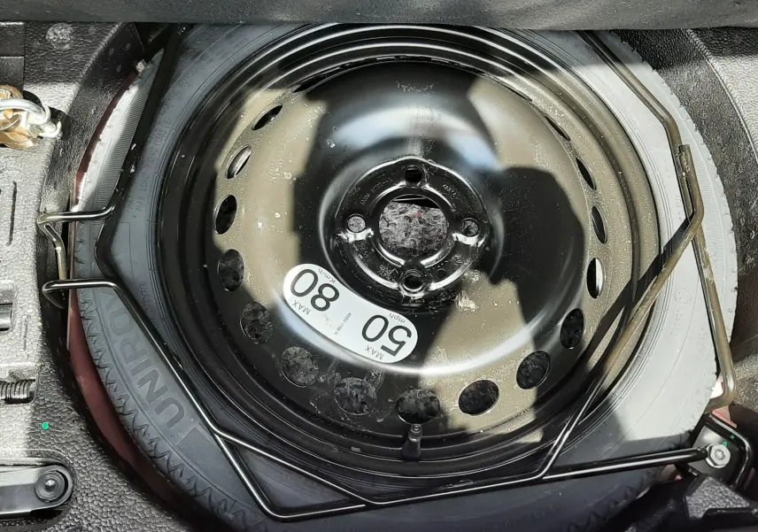 Vue rapprochée de la roue de secours noire dans le coffre de la Renault Clio V rouge flamme 2025.