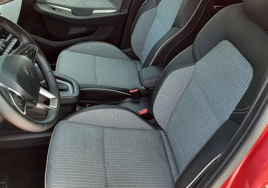 Vue intérieure côté conducteur de la Renault Clio V E-Tech rouge, sièges tissu gris avec surpiqûres blanches et volant cuir.