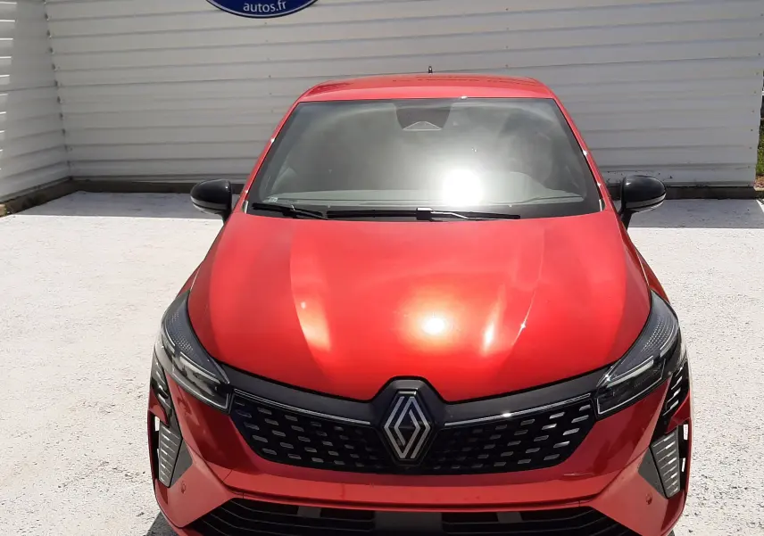 Vue avant d'une Renault Clio V E-Tech Full Hybrid rouge flamme métal avec calandre noire et logo central visible.
