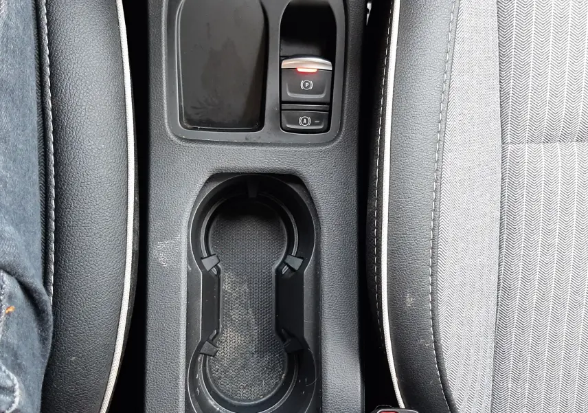 Vue plongeante sur la console centrale noire avec porte-gobelets et boutons de frein à main électrique d’une Renault Clio V rouge flamme.