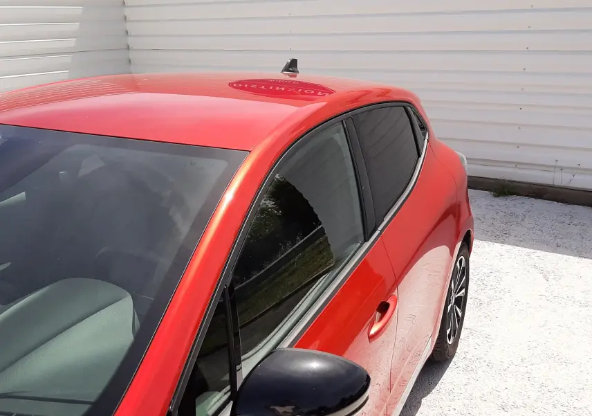 Vue 3/4 avant droit d'une Renault Clio V rouge flamme métal avec rétroviseur noir et vitres teintées.
