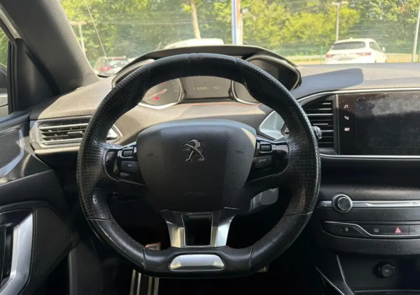 Vue intérieure centrée sur le volant noir perforé de la Peugeot 308 GT-Line 2017 avec tableau de bord et écran tactile.