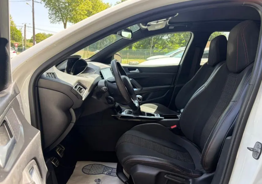 Vue intérieure côté conducteur de la Peugeot 308 GT-Line blanche de 2017, avec sièges noirs et volant multifonction.
