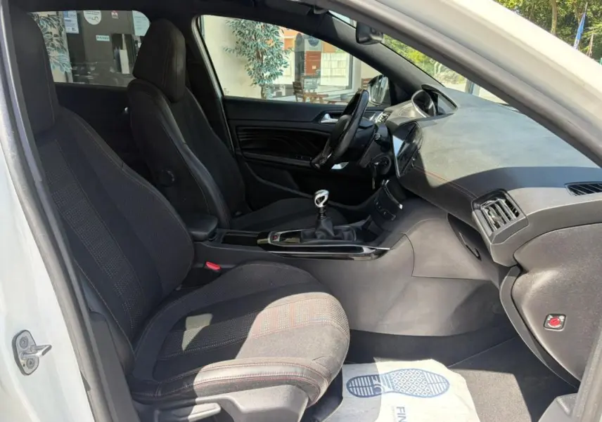 Vue intérieure côté gauche de la Peugeot 308 GT-Line blanche de 2017, avec sièges noirs et levier de vitesse manuel visible.