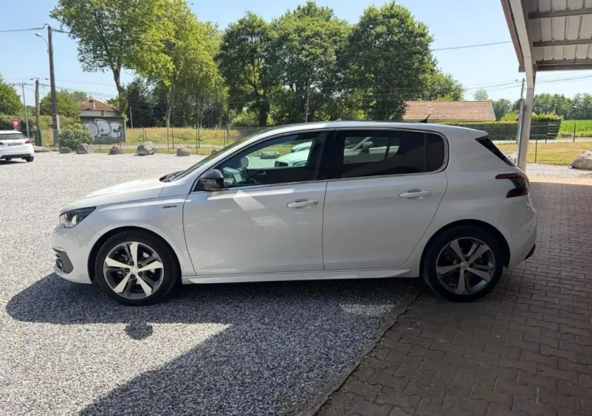 Peugeot 308 GT-Line blanc vue de profil côté gauche, avec jantes alliage et vitres teintées, stationnée à l'ombre.