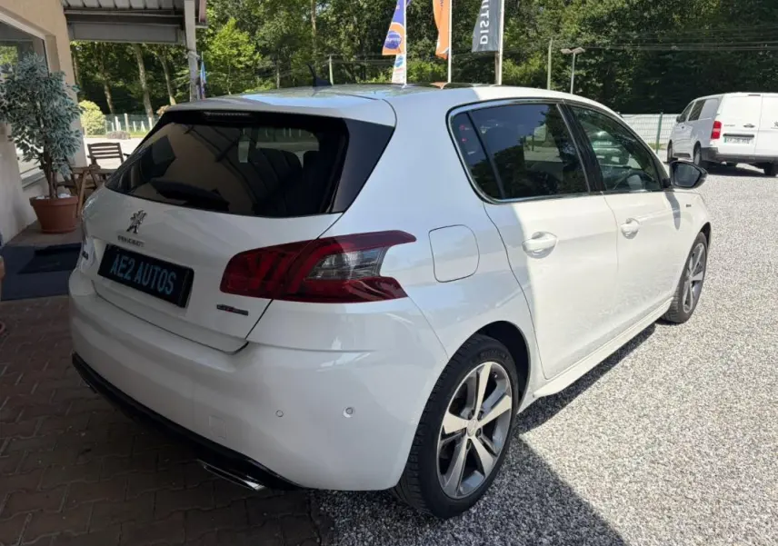 Peugeot 308 GT-Line blanc vue 3/4 arrière droit, avec jantes alliage et vitres teintées, stationnée en extérieur.