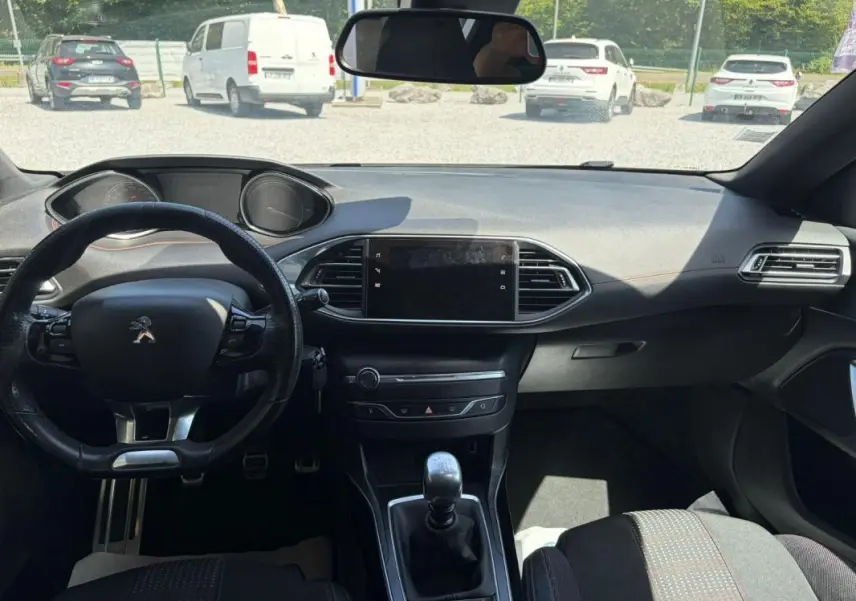 Vue intérieure avant du tableau de bord de la Peugeot 308 GT-Line blanche de 2017 avec volant compact et boîte manuelle.