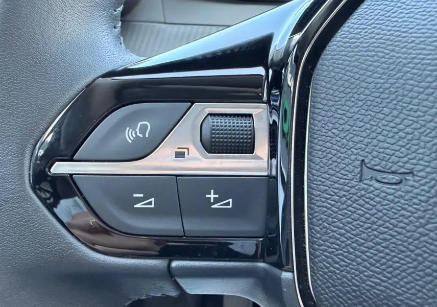 Gros plan sur les commandes noires du volant de la Peugeot 208 1.2 100ch S&S Allure, finition Gris Artense.