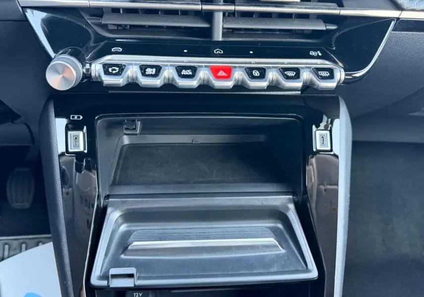 Vue rapprochée de la console centrale noire brillante du Peugeot 208 1.2 100ch, avec boutons de commande et prise USB.