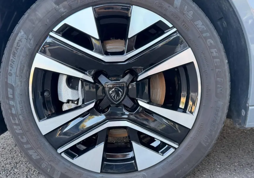 Gros plan sur la jante alu bicolore noire et argentée d'une Peugeot 208 Gris Artense avec logo lion central.