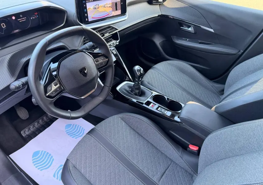 Vue intérieure côté conducteur de la Peugeot 208 1.2 100ch gris Artense, volant compact et écran tactile central visible.