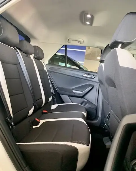 Vue intérieure arrière côté droit du Volkswagen T-Roc blanc 2021, sièges noirs avec surpiqûres claires et ceinture blanche.