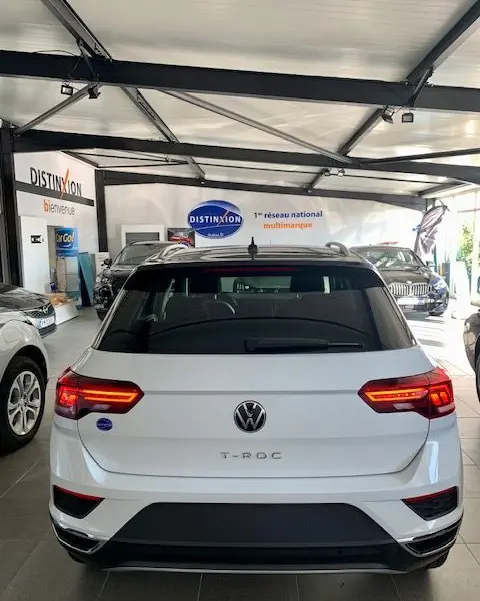 Vue arrière d'un Volkswagen T-Roc blanc 2021 en showroom, avec feux LED allumés et toit noir contrastant.