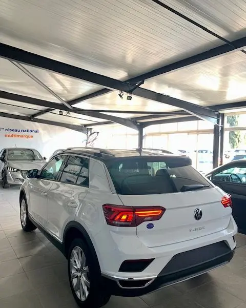 Vue 3/4 arrière droite d'un Volkswagen T-Roc blanc 2021 en showroom avec feux arrière allumés.