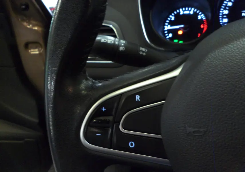 Gros plan sur le volant noir de la Renault Mégane IV TCe 100 CH LIFE, avec commandes intégrées et tableau de bord éclairé.