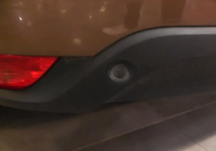 Gros plan sur le capteur de recul arrière intégré dans le pare-chocs noir d'une Renault Mégane IV brun cappuccino.