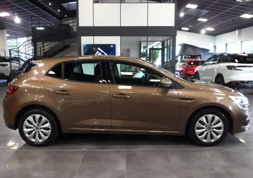 Profil côté droit d'une Renault Mégane IV TCe 100 Life brun cappuccino dans un showroom lumineux.
