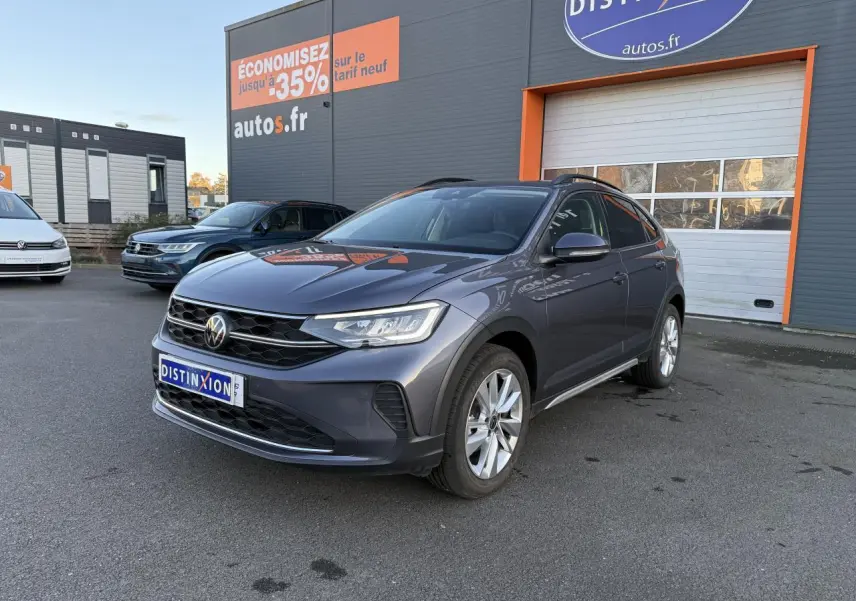 Volkswagen Taigo 2025 gris INC en 3/4 avant droit, avec jantes alliage et toit noir visible devant un bâtiment commercial.