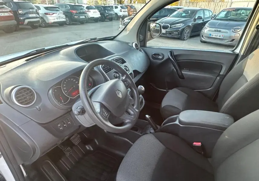 Vue intérieure côté conducteur du Renault Kangoo Express blanc, montrant le tableau de bord et les sièges noirs.