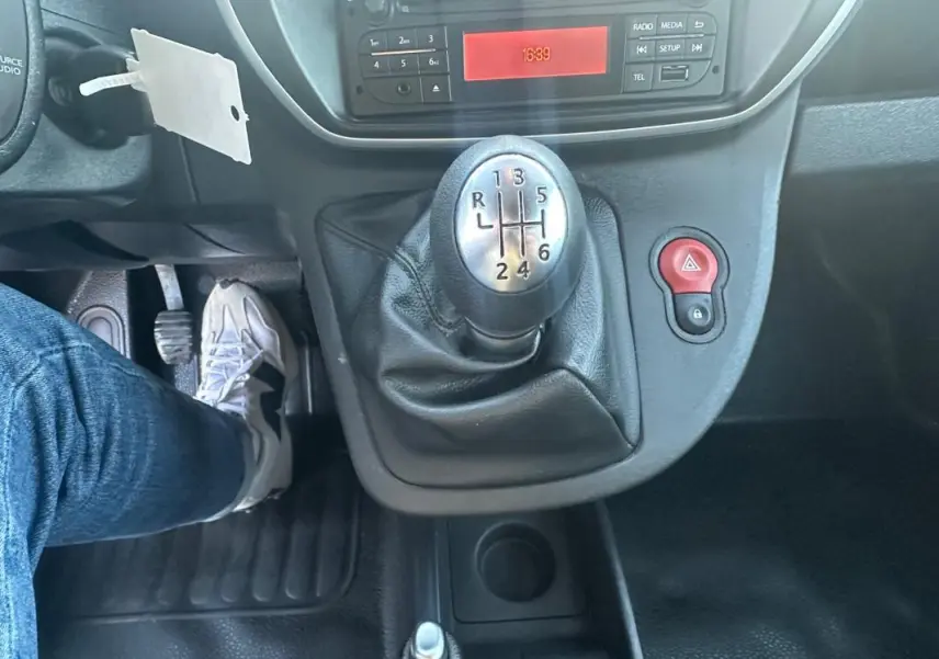 Gros plan sur le levier de vitesses manuelle à six rapports du Renault Kangoo Express blanc, avec tableau de bord et pédales visibles.