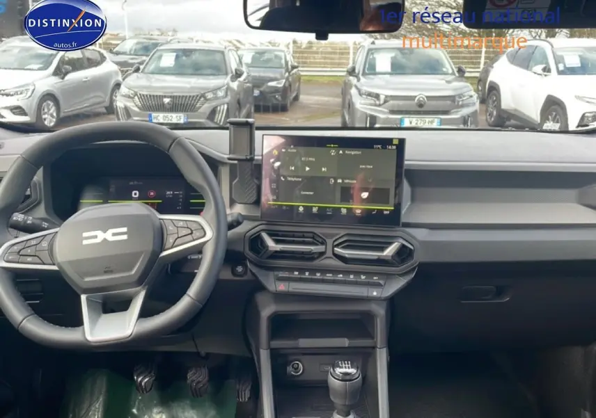 Vue intérieure du tableau de bord du Dacia Duster 2026 vert cèdre, avec volant multifonction et écran tactile central.