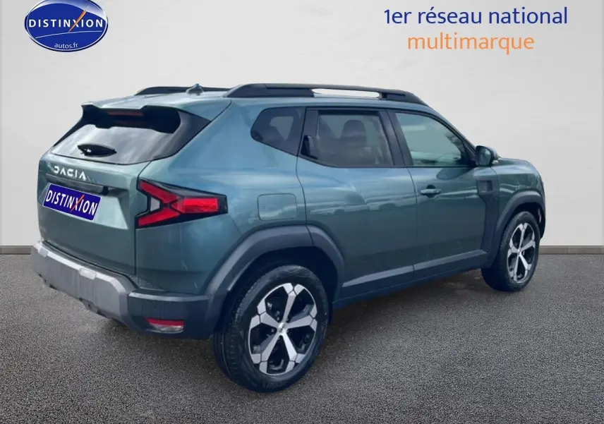 Vue 3/4 arrière droite du Dacia Duster 2026 vert cèdre avec jantes alu et barres de toit noires.