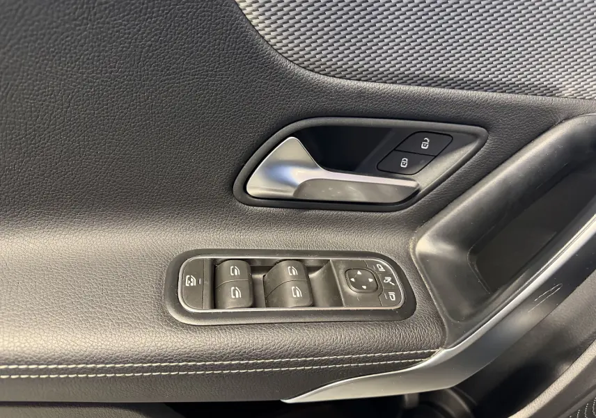 Gros plan sur la porte intérieure côté conducteur d'une Mercedes Classe A noire, avec commandes de vitres et poignée argentée.
