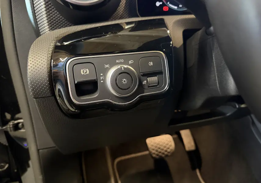 Gros plan sur le panneau de commande des phares et frein à main électrique dans l'habitacle noir d'une Mercedes Classe A 2022.