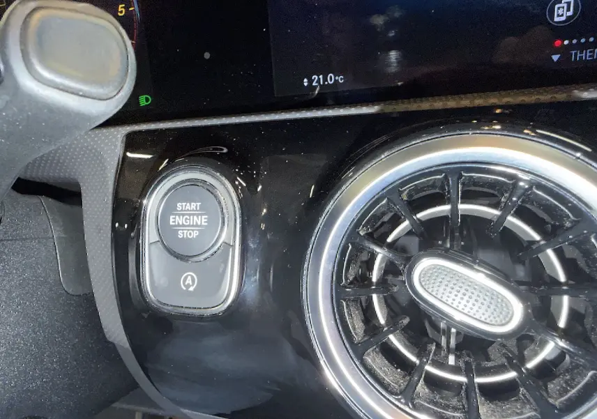 Détail intérieur montrant le bouton Start/Stop et la sortie d'air ronde chromée d'une Mercedes Classe A noire.