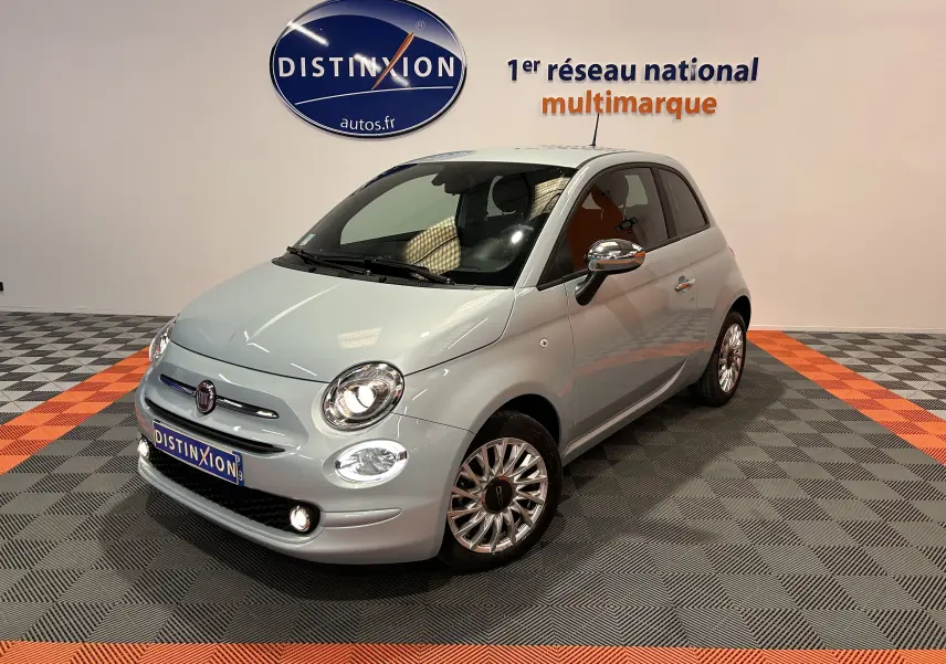 Vue 3/4 avant d'une Fiat 500 gris clair avec jantes alliage et rétroviseurs chromés en showroom.